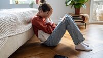 Unhappy teen girl covering face with hands crying while sitting on floor with mobile phone nearby